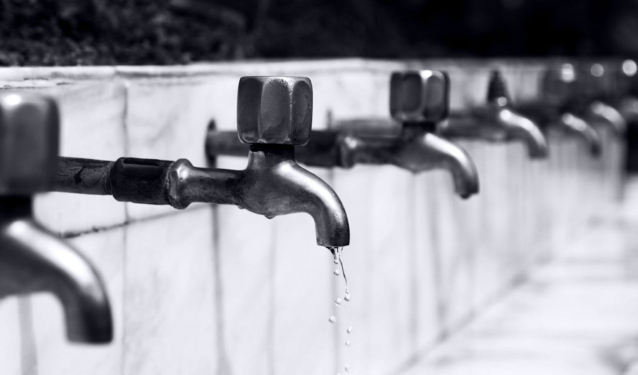 services-06 Black and white image of a row of faucets with water dripping, highlighting plumbing details.